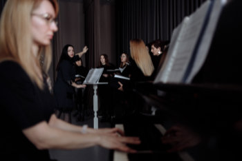 Singen im Chor Frau am Klavier mit Chor und Dirigentin im Hintergrund